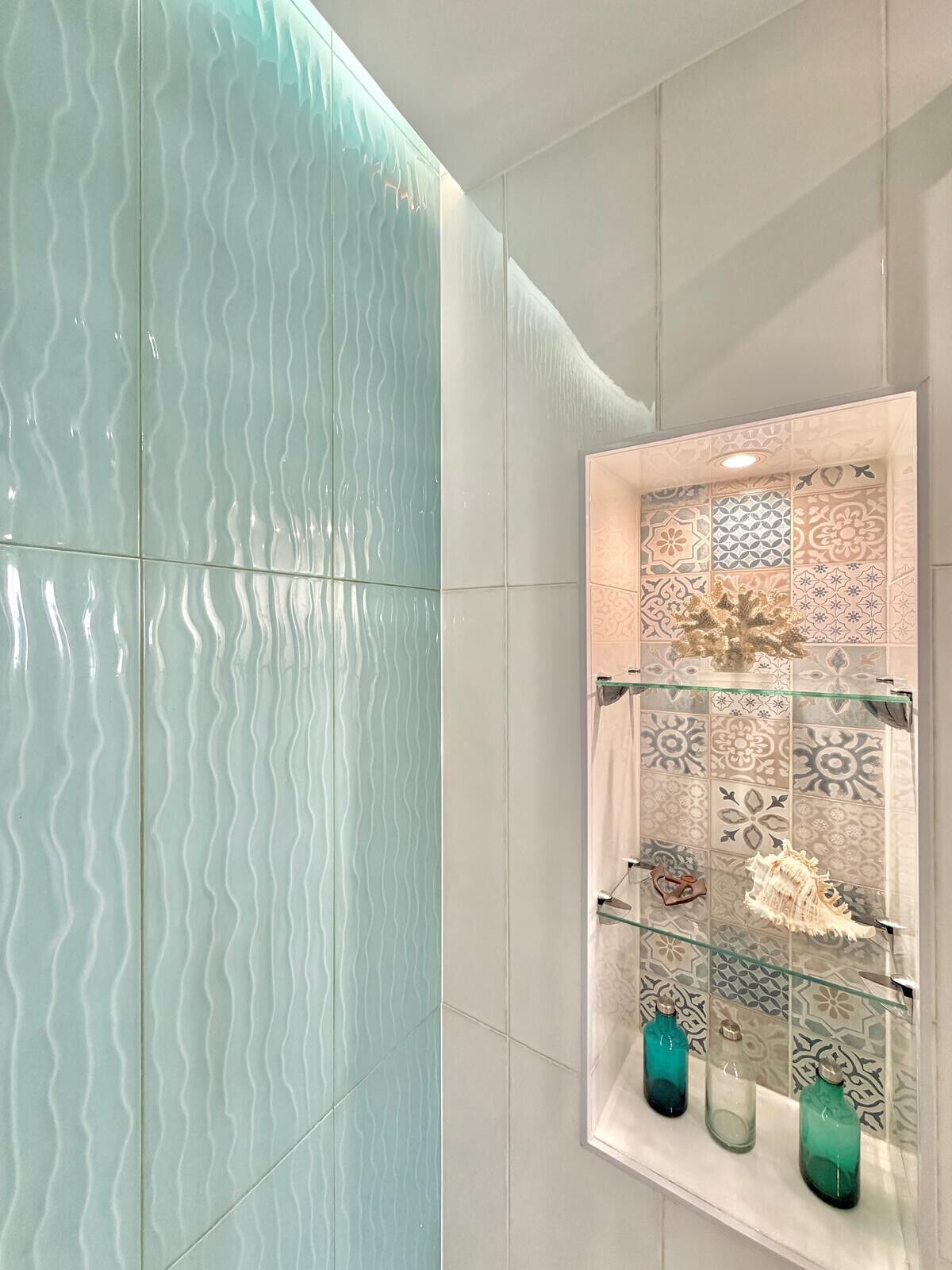 Un bagno con un divisorio in vetro ondulato, una parete rivestita di piastrelle con motivo floreale e mensole con oggetti decorativi.