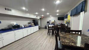 A kitchen with white cabinets, a microwave, a coffee machine, and a dining area with a marble table and chairs.