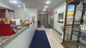 A hotel corridor with a reception area, a blue carpet, a glass display case with flowers, and an American flag decoration.