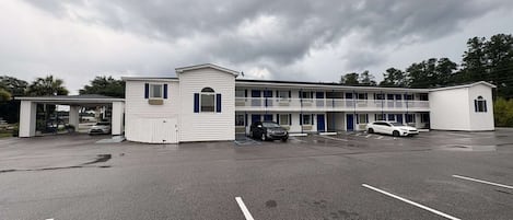 Un motel composé d’un bâtiment principal et de deux annexes plus petites, d’un espace de stationnement couvert et d’un grand parking extérieur.