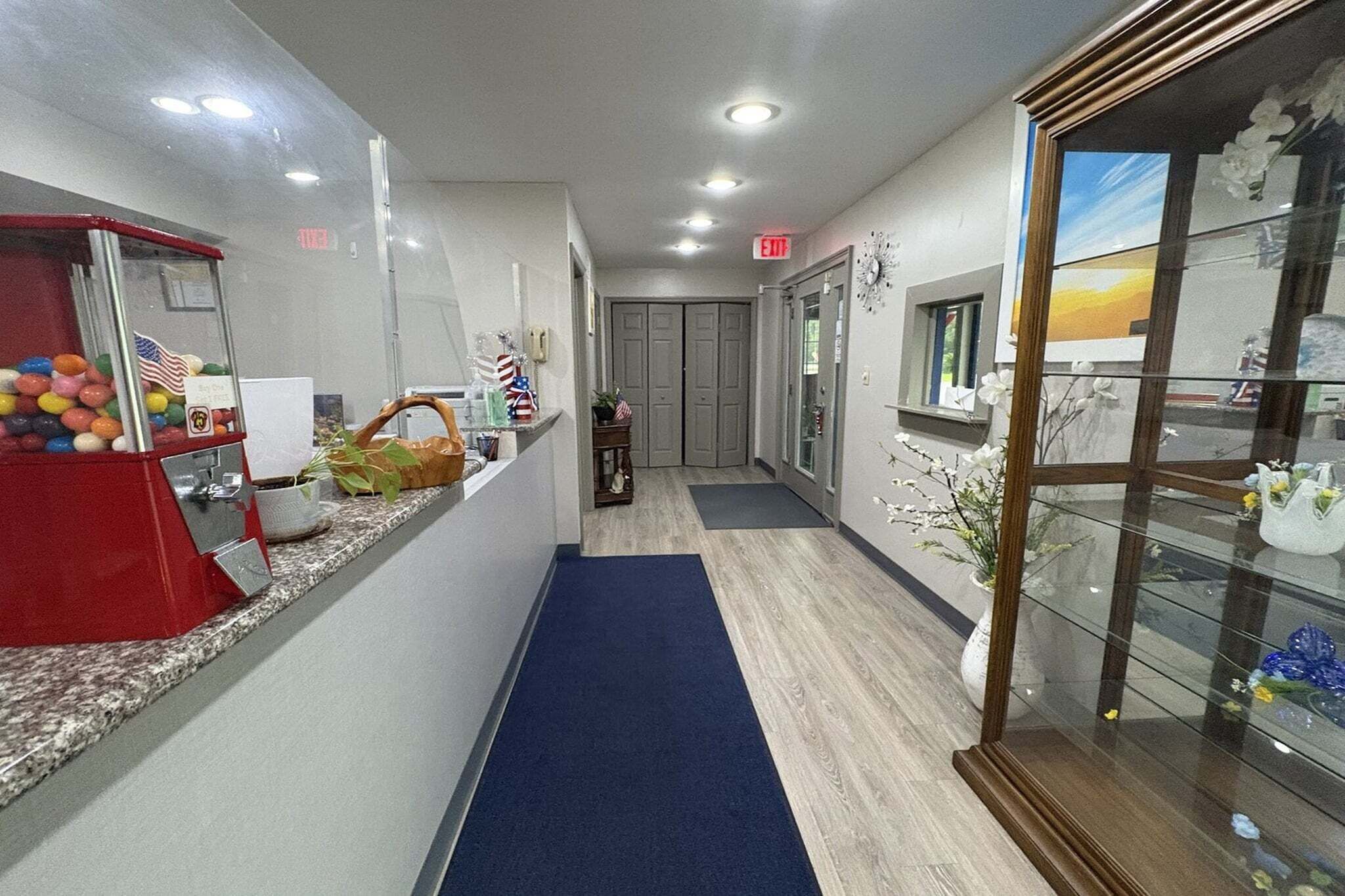 A hotel corridor with a reception area, a blue carpet, a glass display case with flowers, and an American flag decoration.
