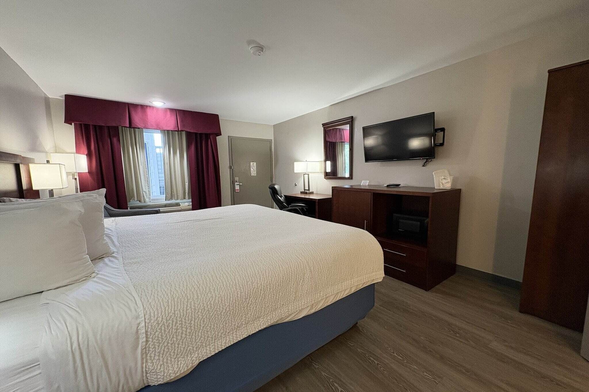 Una habitación de hotel con una cama grande, un escritorio, una silla, un televisor y un armario.