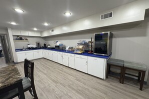 A kitchen with white cabinets, a blue countertop, a refrigerator, and a dining area with a table and chairs.