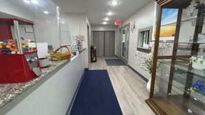 A hotel reception area with a blue carpet, a red vending machine, and a glass display case with flowers.