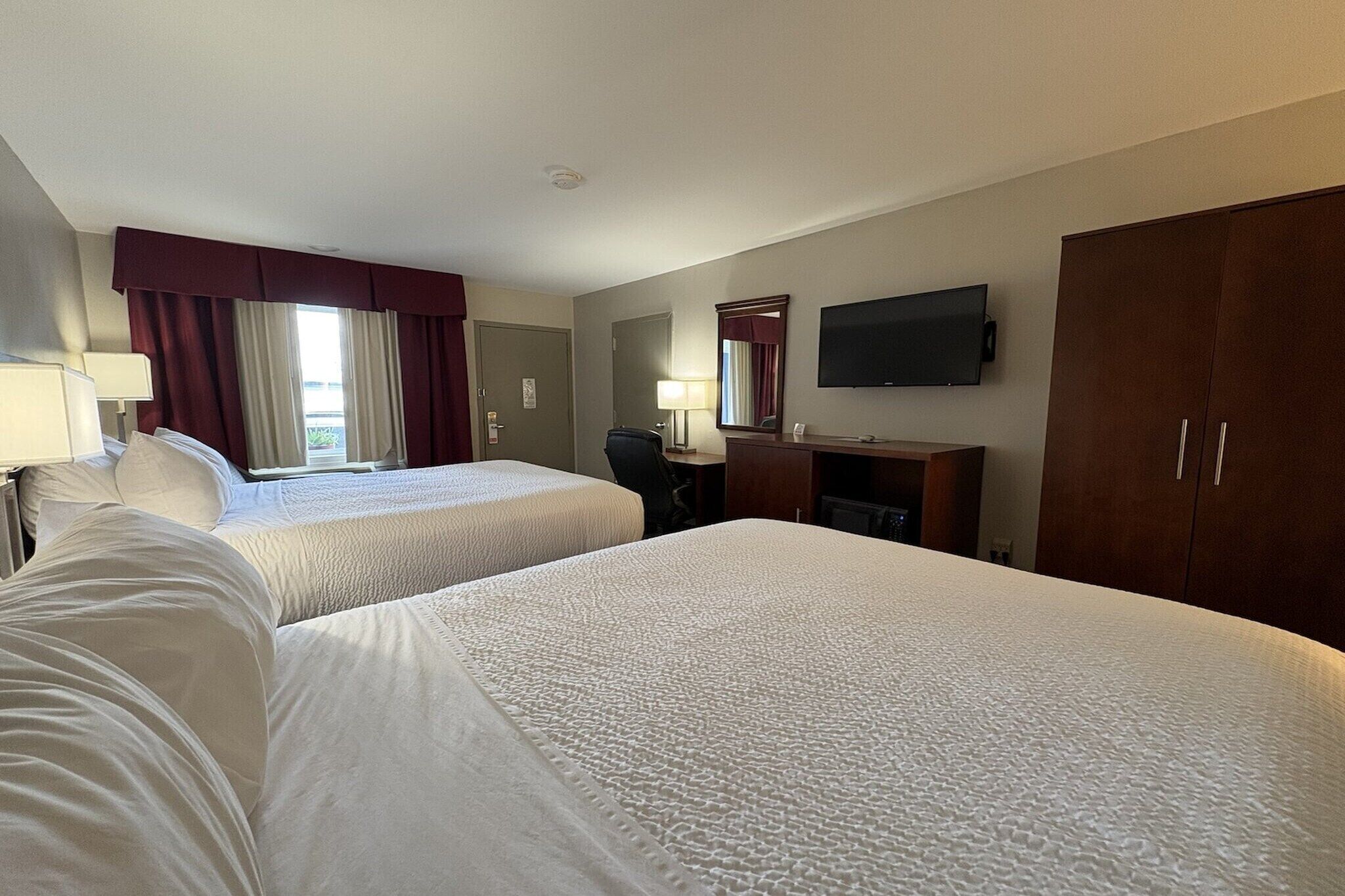 A hotel room with two beds, a desk, a TV, and a wardrobe.