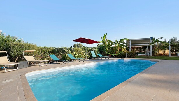 A swimming pool with lounge chairs and a red umbrella.