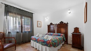 A bedroom with a bed, a chair, a wooden cabinet, and a window with curtains.