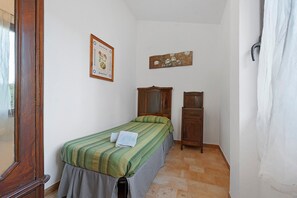 A small, narrow room with a single bed, a wooden cabinet, and a framed botanical illustration on the wall.
