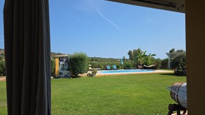 A clear view of a swimming pool, green lawn, and a building with a yellow facade. - Apartment 'Masone Verde' with Shared Pool, Wi-Fi and Air Conditioning (Castiadas)