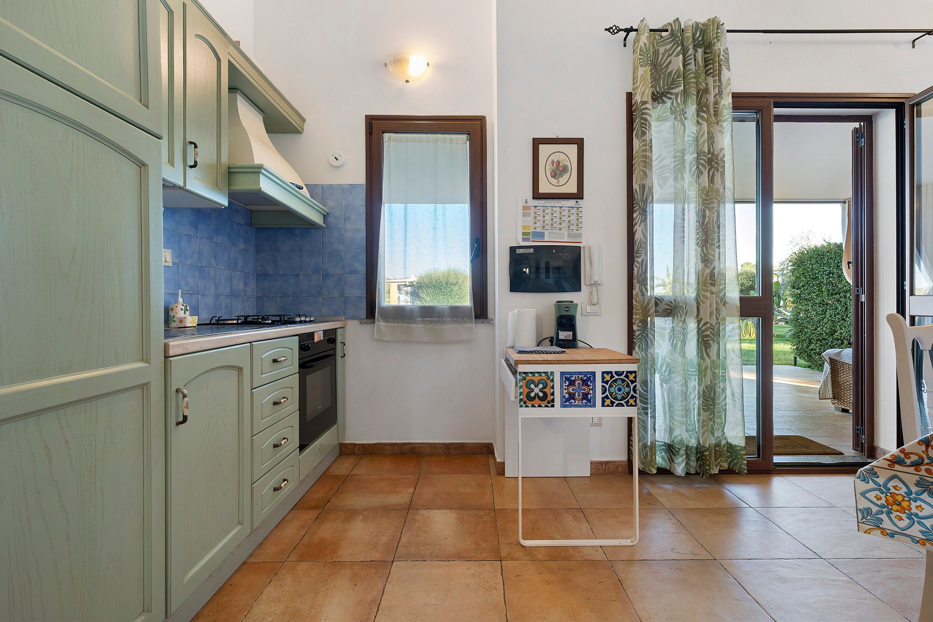 Une cuisine équipée d’une cuisinière, d’un four et de placards, une fenêtre avec vue et une petite table sur laquelle se trouvent un téléphone et des papiers.