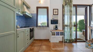 Une cuisine équipée d’une cuisinière, d’un four et de placards, une fenêtre avec vue et une petite table sur laquelle se trouvent un téléphone et des papiers.