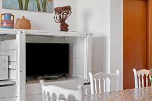 A room with a white brick fireplace, a television, and white furniture.