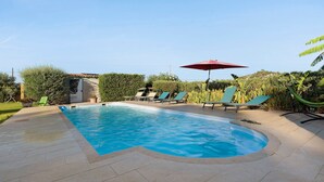 A swimming pool with a curved edge, surrounded by lounge chairs and a red umbrella.