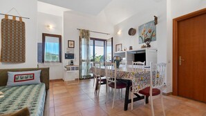 A cozy room with a bed, a dining table, chairs, a kitchen area, and a door.