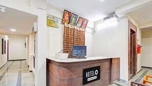 A hotel reception desk with a sign reading 'HOTELO Company Serviced,' a computer, and framed pictures on the wall. - Classic Agp Home Stay (Chennai)