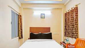 A hotel room with a bed, a chair, a small table, and a window with curtains. - Classic Agp Home Stay (Chennai)