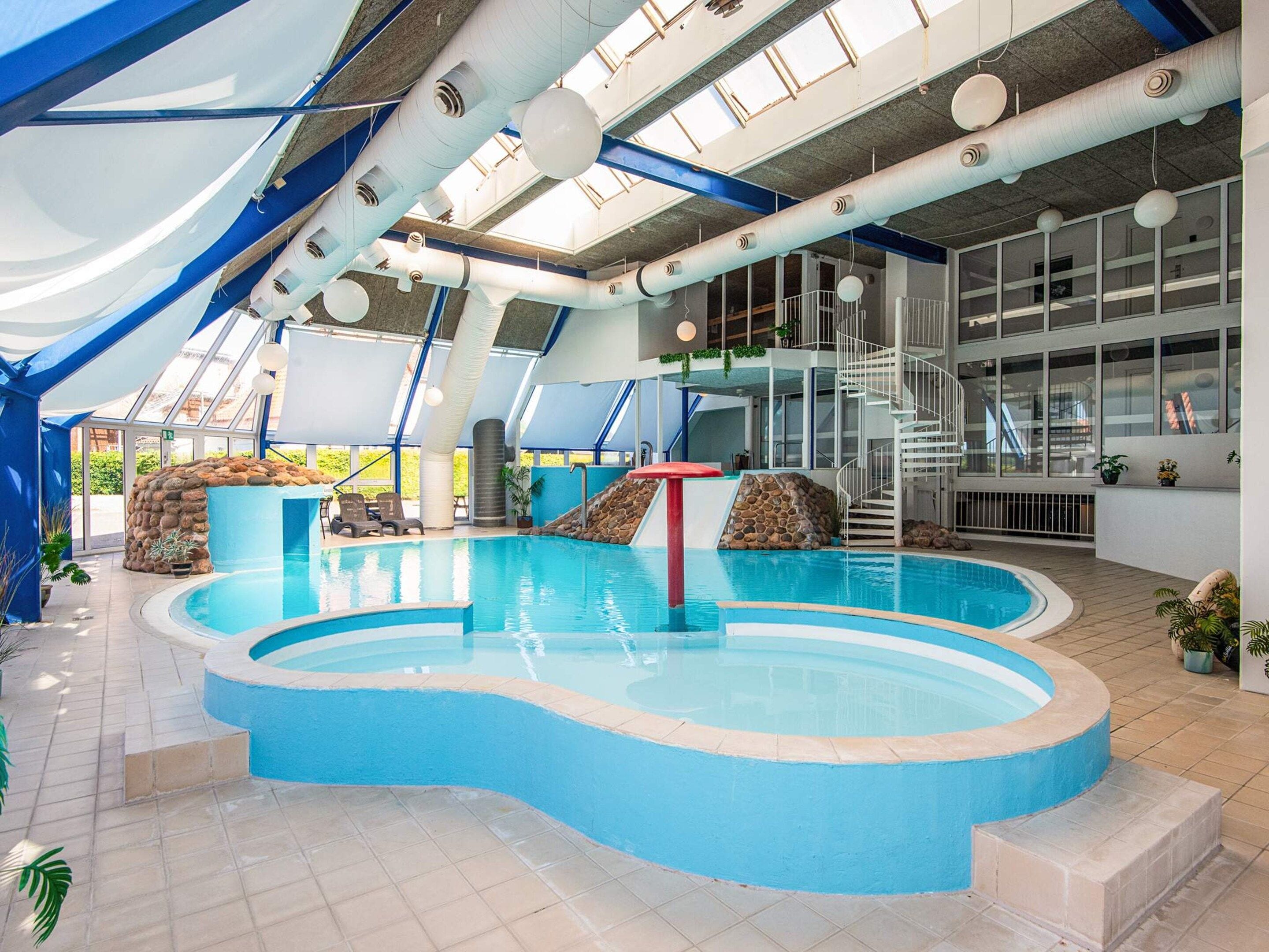An indoor swimming pool with a blue border, a rock feature, and a staircase leading to an upper level.