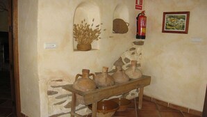 Un interior rústico con una pared de piedra, un banco de madera con cerámica, un extintor y un cuadro enmarcado.