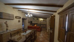 Una cocina rústica con una mesa de comedor, sillas de madera, chimenea y una araña.