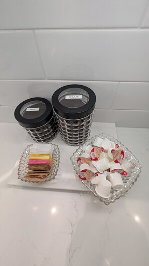 Three glass containers with lids, a glass tray with coffee packets, and a glass dish with coffee capsules. - NEW! Historic, Walk to Main St, King Suites, Patio (Madison)