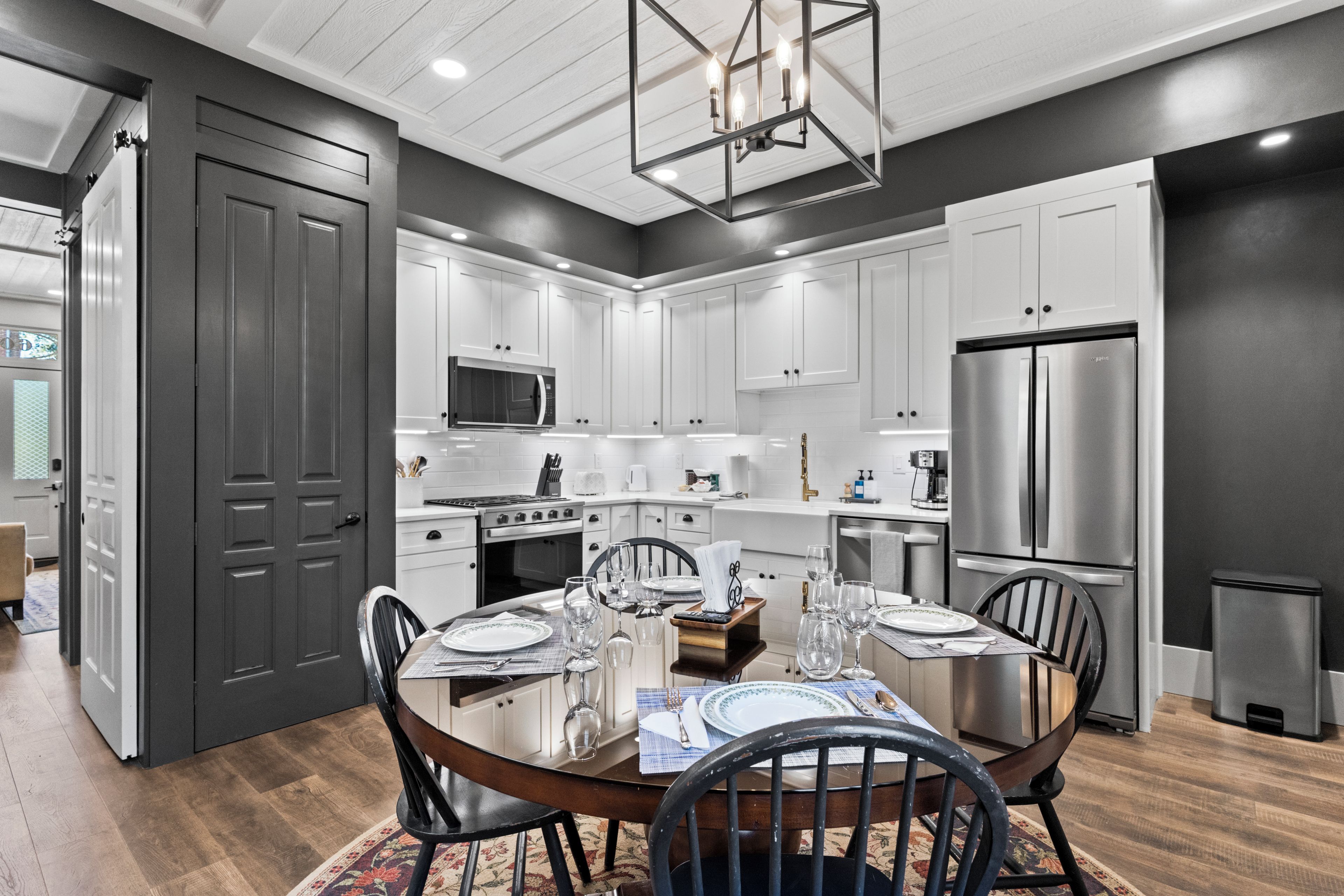 A modern kitchen with white cabinetry, stainless steel appliances, and a dining area set for four.