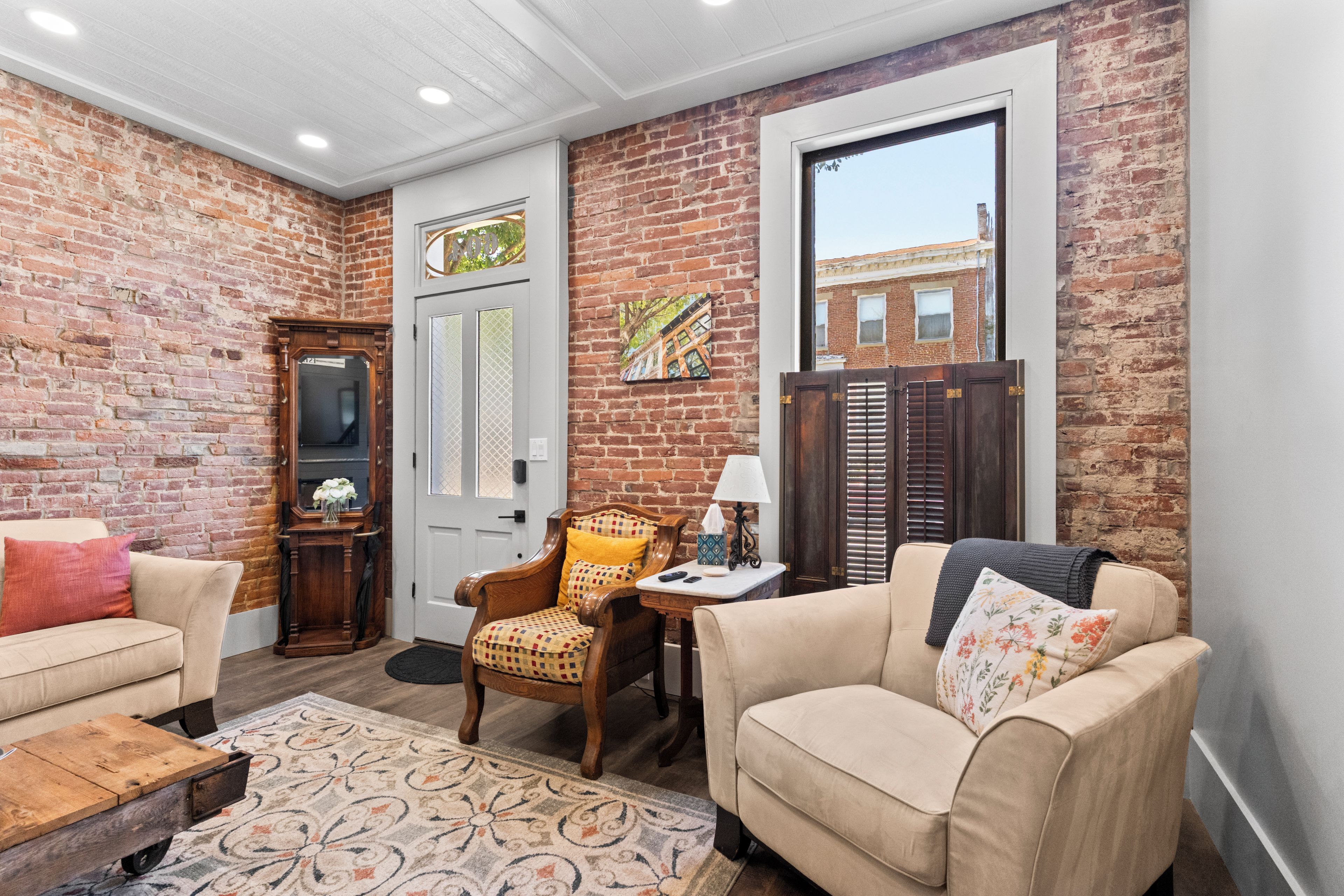 A cozy room with a brick wall, a white door, a wooden chair, a beige sofa, and a small table with a lamp.