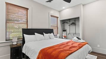 A bedroom with a bed, a nightstand, a lamp, a ceiling fan, and a walk-in closet with hanging clothes.