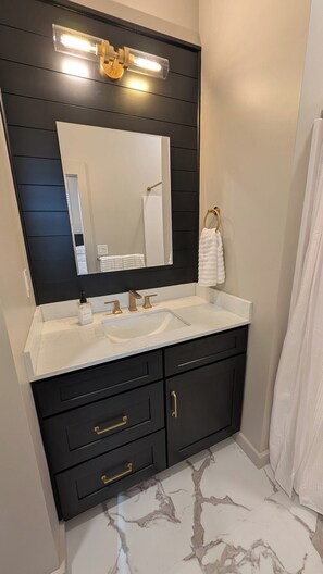 A bathroom with a dark vanity, white sink, gold fixtures, a large mirror, and a white towel. - NEW! Historic, Walk to Main St, King Suites, Patio (Madison)