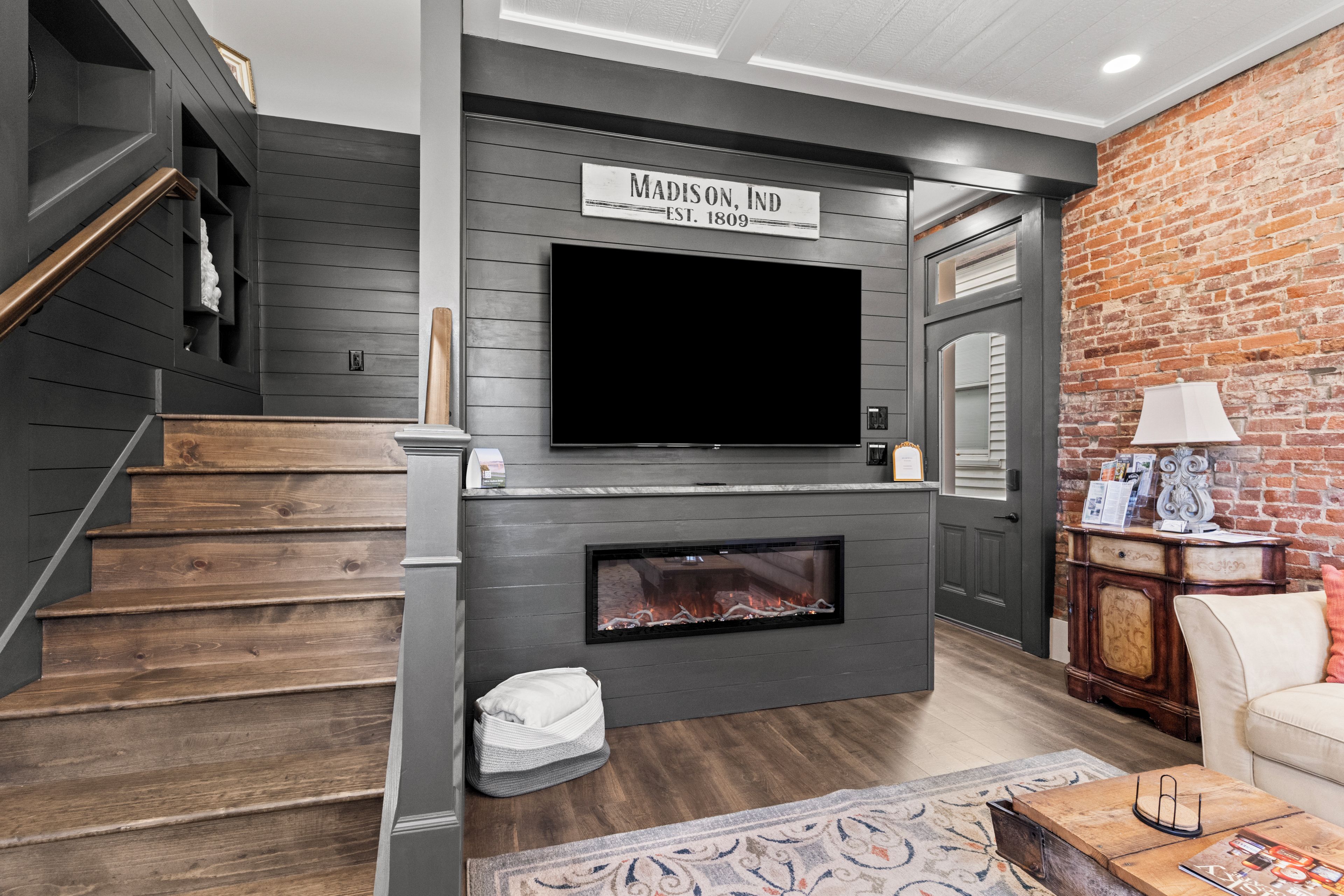 A modern living room with a fireplace, a flat-screen TV mounted above it, and a staircase with wooden steps.