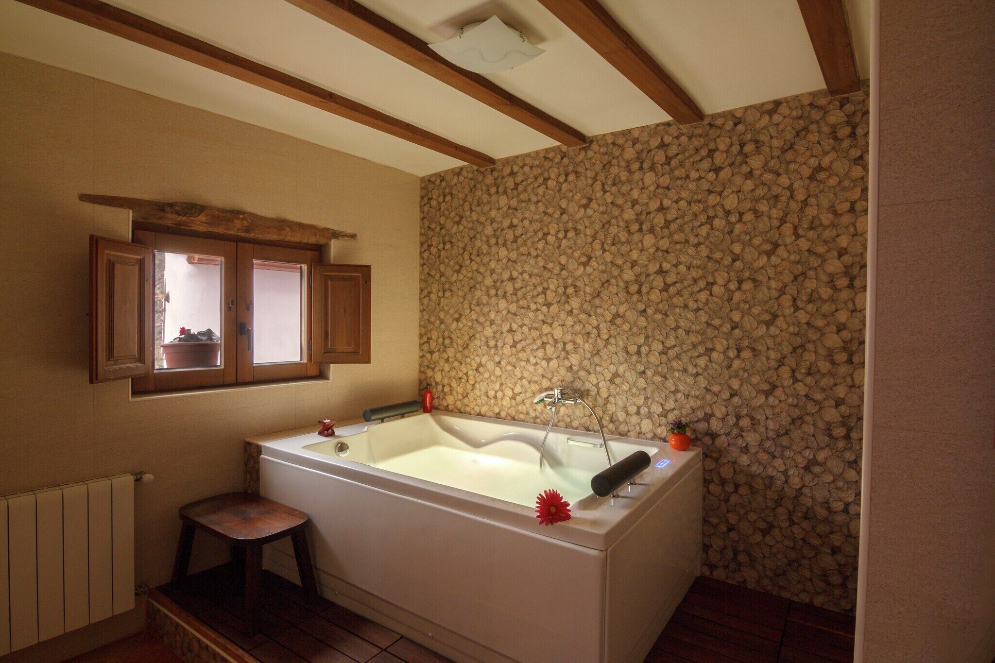 Un baño con bañera, vigas de madera, pared de piedra, ventana y radiador.