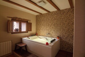 Une salle de bain avec une baignoire, des poutres en bois, un mur en pierre, une fenêtre et un radiateur.