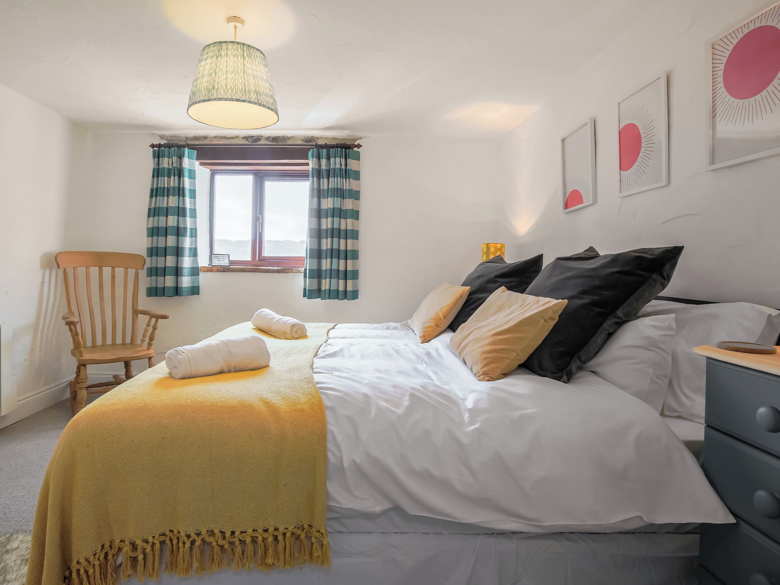 A bedroom with a bed, a chair, a window with curtains, and wall art.