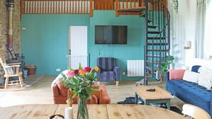 A living room with a wooden ceiling, a TV mounted on the wall, a sofa, a chair, a table, and a staircase. - 3 bedroom accommodation in Dulverton (Dulverton)