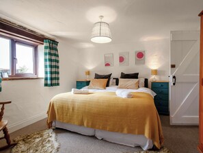 Une chambre à coucher avec un lit, des tables de chevet, une fenêtre avec des rideaux, une porte et des œuvres d’art murales.