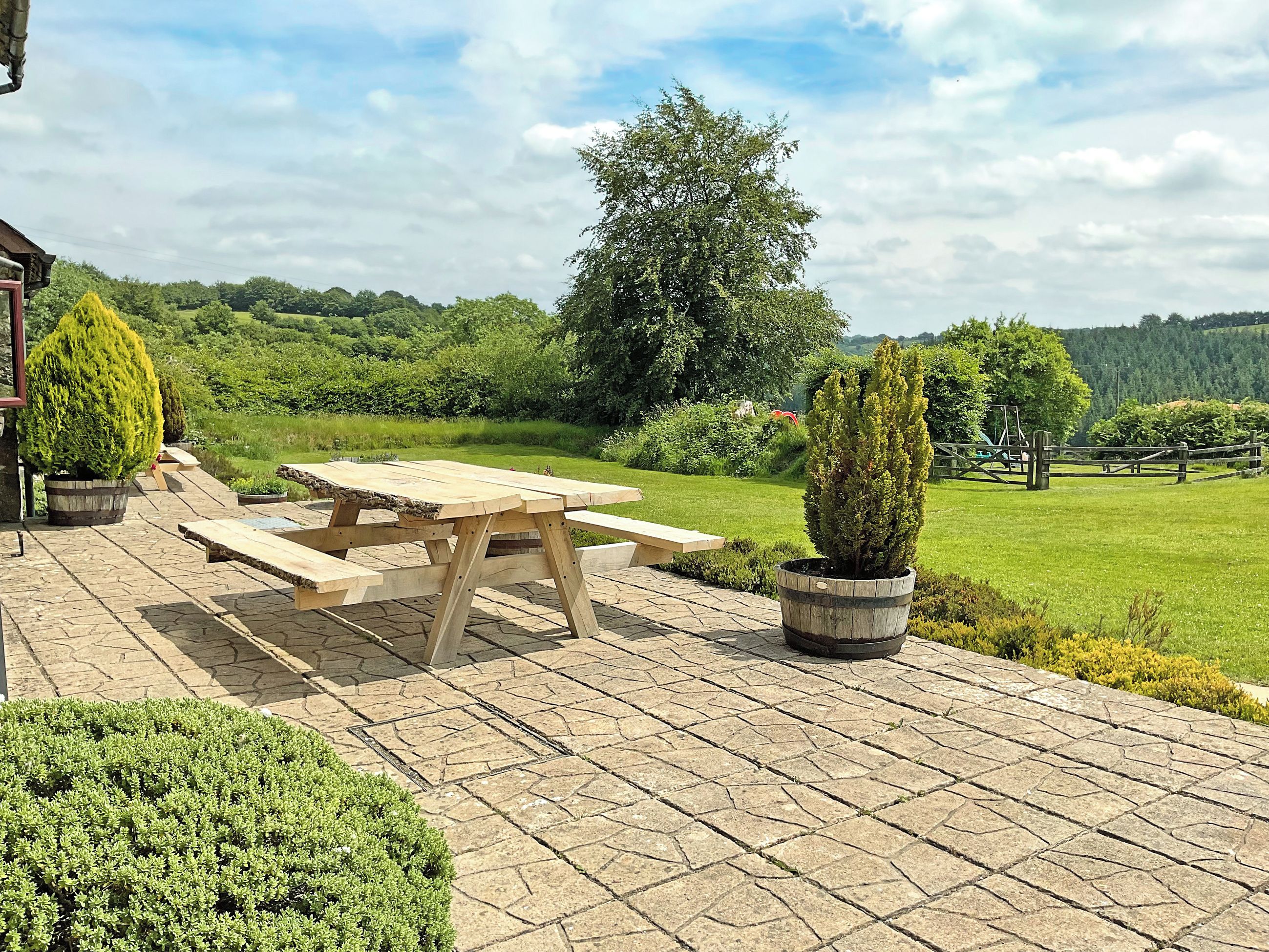 A picnic table with benches on a paved patio with potted plants.