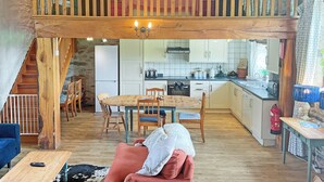 A spacious loft-style living area with a high ceiling, wooden beams, a dining table, and a kitchen in the background. - 3 bedroom accommodation in Dulverton (Dulverton)