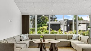 Una sala moderna con un sofá modular, dos mesas redondas y grandes ventanales que ofrecen vistas al exterior.