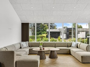 Una sala moderna con un sofá modular, dos mesas redondas y grandes ventanales que ofrecen vistas al exterior.