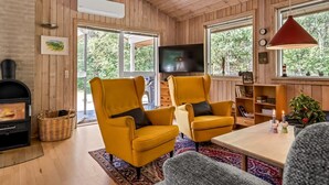 A wooden-paneled room with a fireplace, two yellow armchairs, a television, and a large window. - "Laris" -  from the sea by Interhome (Hadsund)