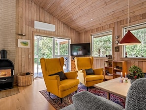 Ein Zimmer mit Holzwänden, einem Kamin, zwei gelben Sesseln, einem Fernseher und einem großen Fenster.