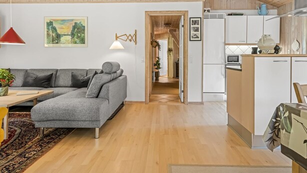 A modern interior with a grey sectional sofa, a red pendant light, and a kitchen area with white cabinets and a microwave. - "Laris" -  from the sea by Interhome (Hadsund)