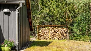 A wooden shed with a metal roof, a stack of firewood, and a garden with flowers. - "Laris" -  from the sea by Interhome (Hadsund)