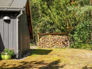 Ein Holzschuppen mit Metalldach, ein Holzstapel und ein Garten mit Blumen.