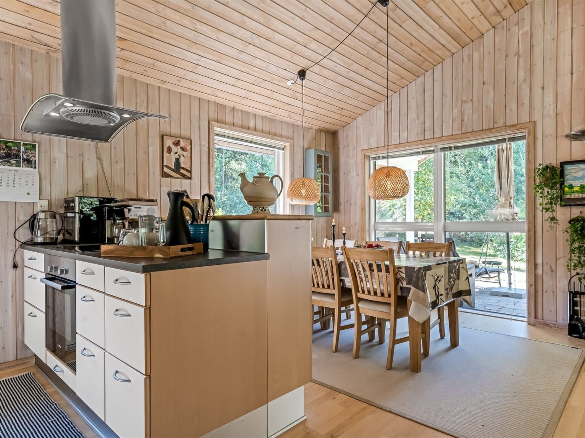 A modern kitchen with wooden walls, a dining area with wooden chairs, and large windows.