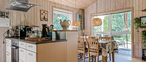 A modern kitchen with wooden walls, a dining area with wooden chairs, and large windows.