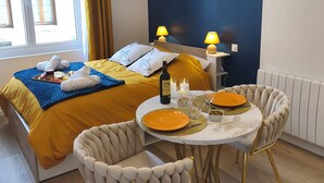 A bedroom with a bed, bedside lamps, a bedside table with a bottle and glasses, and a dining area with a table and chairs. - Le Saphir d'Ault—The beach is 100 meters away, and restaurants are just a stone's throw away (Ault)