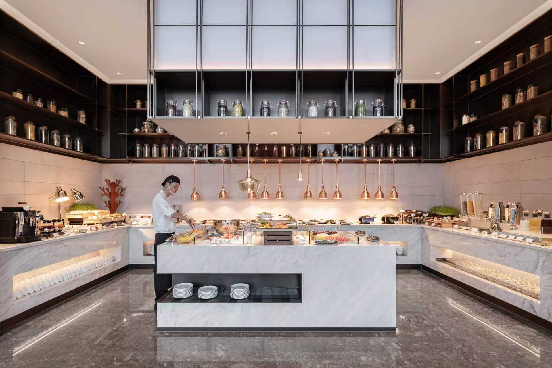 Een moderne keuken met een centraal eiland, bovenkasten en een kok die aan het koken is.