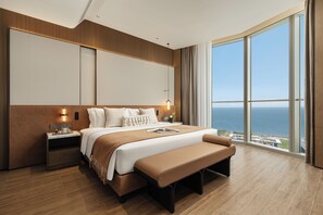A modern hotel room with a large bed, a bench, a nightstand, and a view of the sea. - Ascott East Coast Haikou (Haikou)