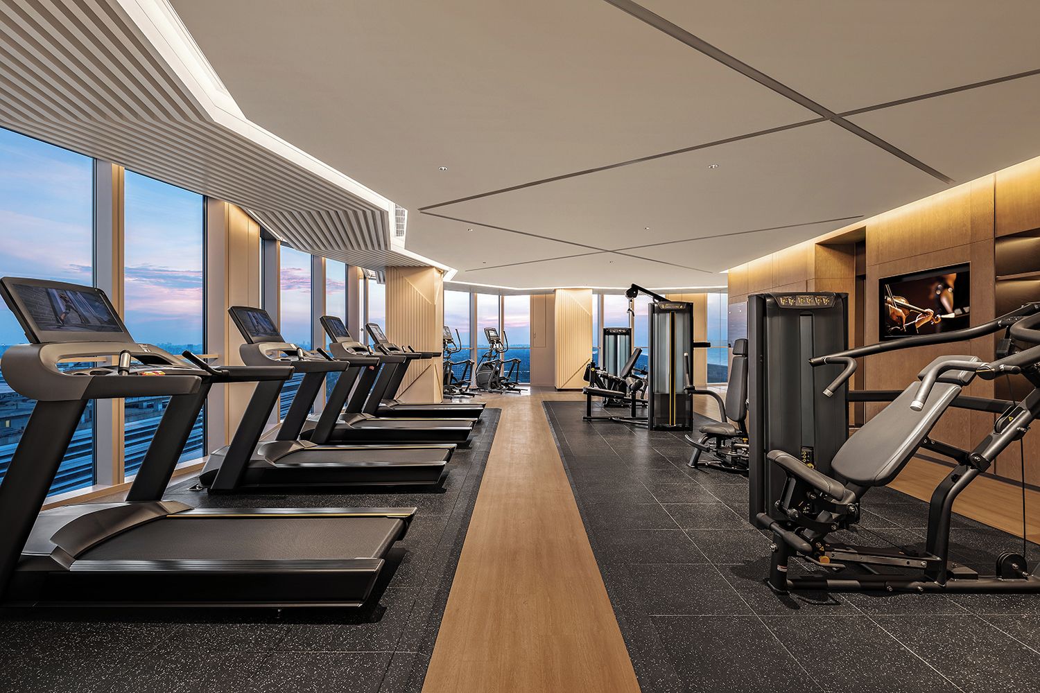 A modern gym with treadmills, weight machines, and a view of the city.