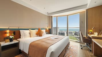 A modern hotel room with a large bed, a desk, and a view of the city.